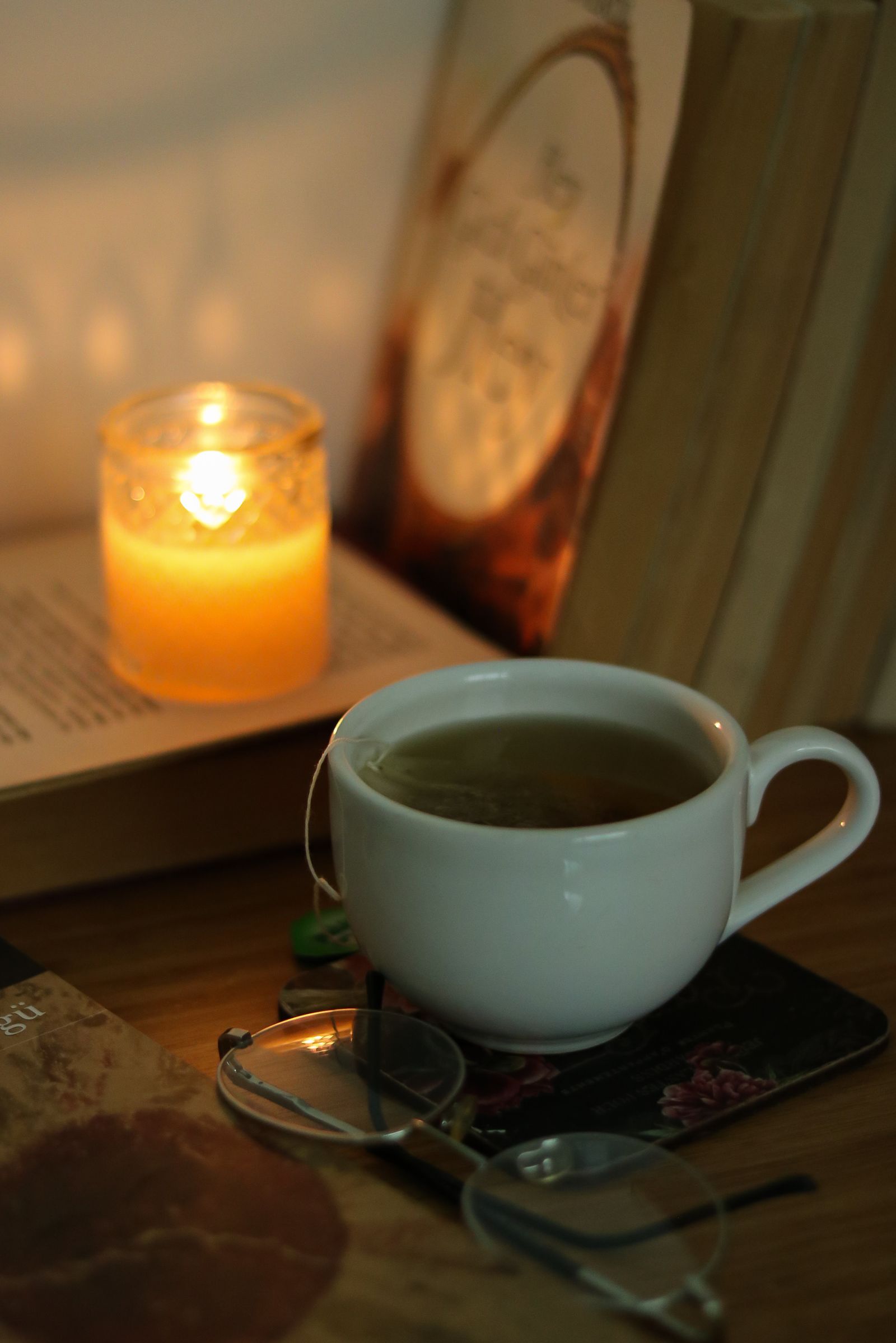 A warm reading corner with a lit candle, cup of tea, and glasses for a wind-down routine