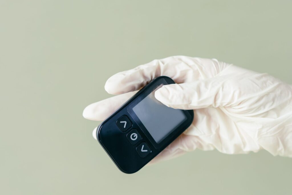 A hand in latex gloves holding a blood glucose meter