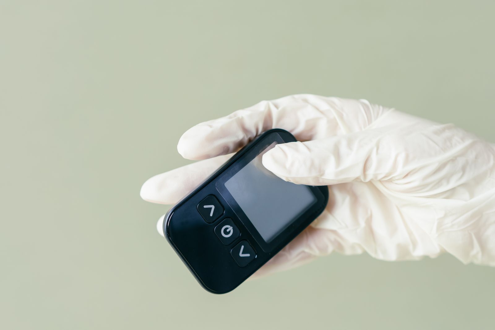 A hand in latex gloves holding a blood glucose meter