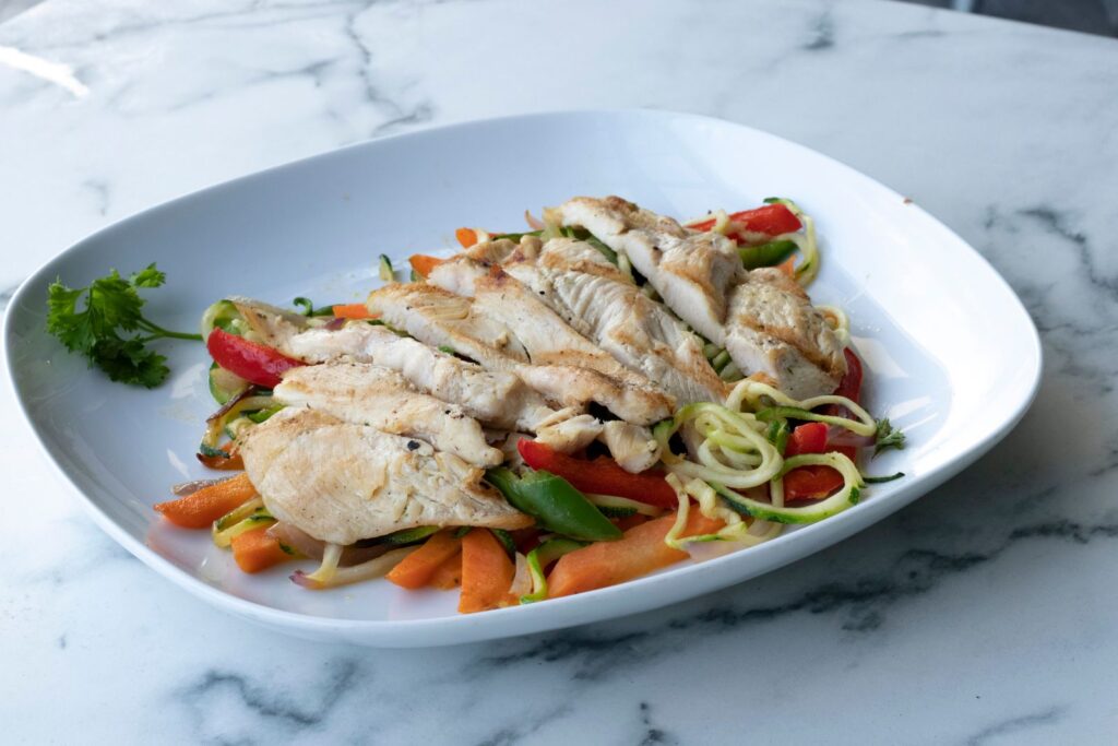 Healthy grilled chicken breast served on zucchini noodles and fresh vegetables