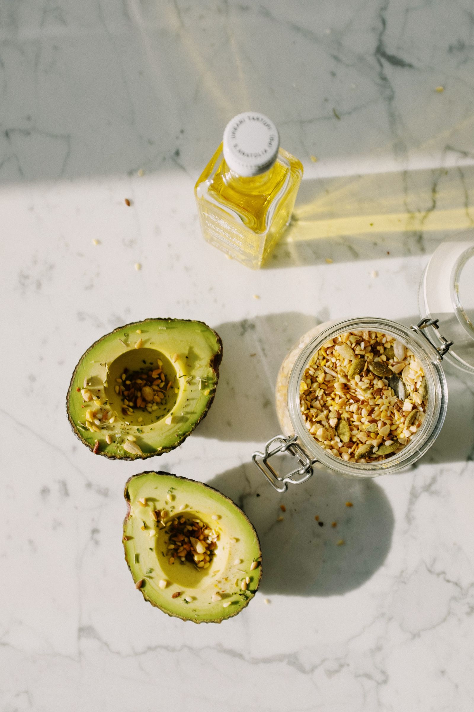 Fresh avocado halves with seeds and olive oil on a marble surface