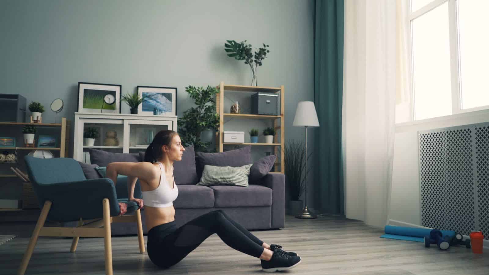 A woman doing tricep dips at home using a chair for support