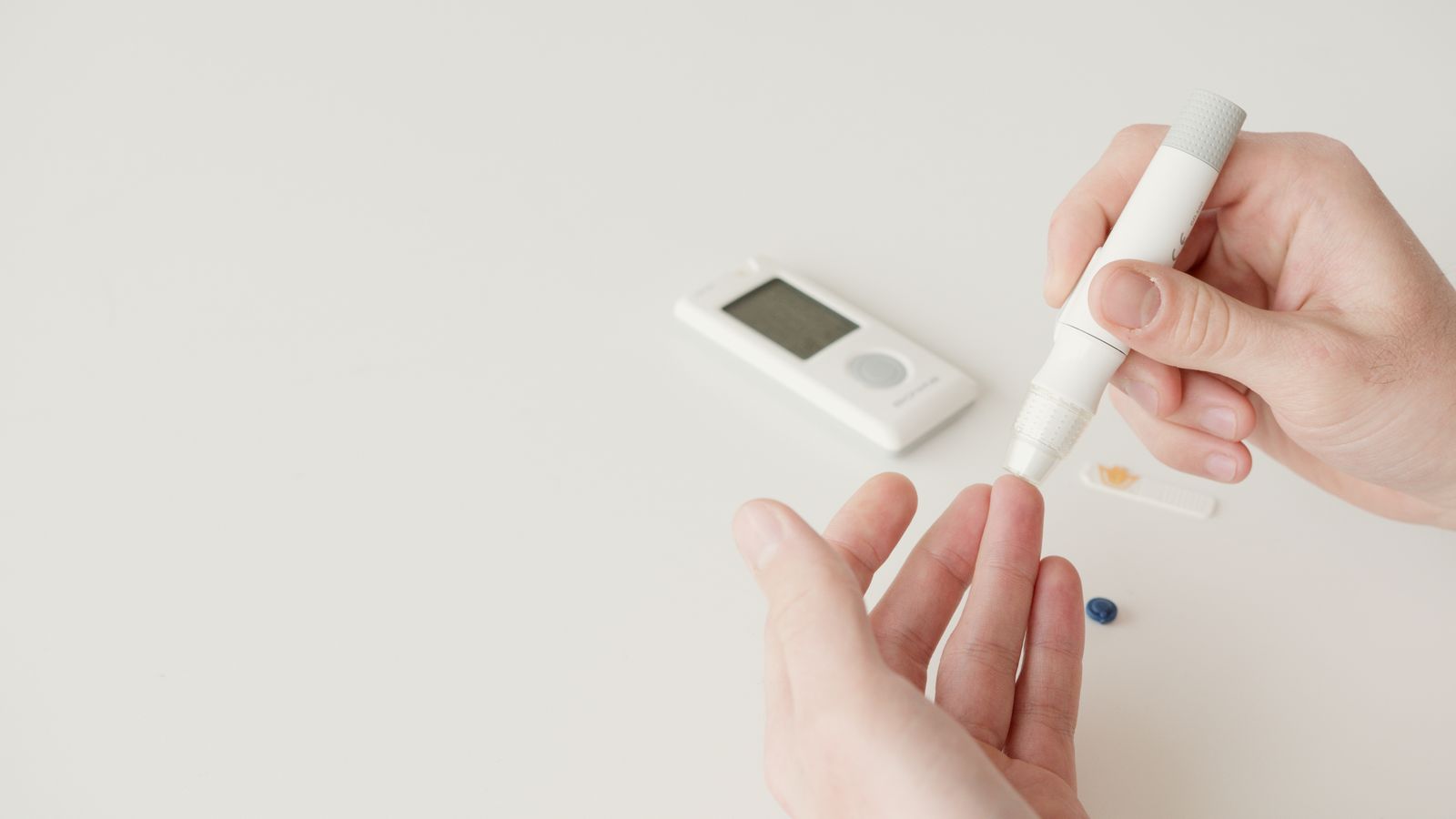 Hands using a lancet pen and glucometer for blood sugar testing