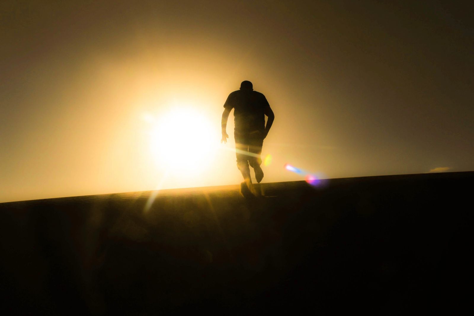 Silhouette of a man running uphill against a bright desert sunrise, capturing solitude and determination