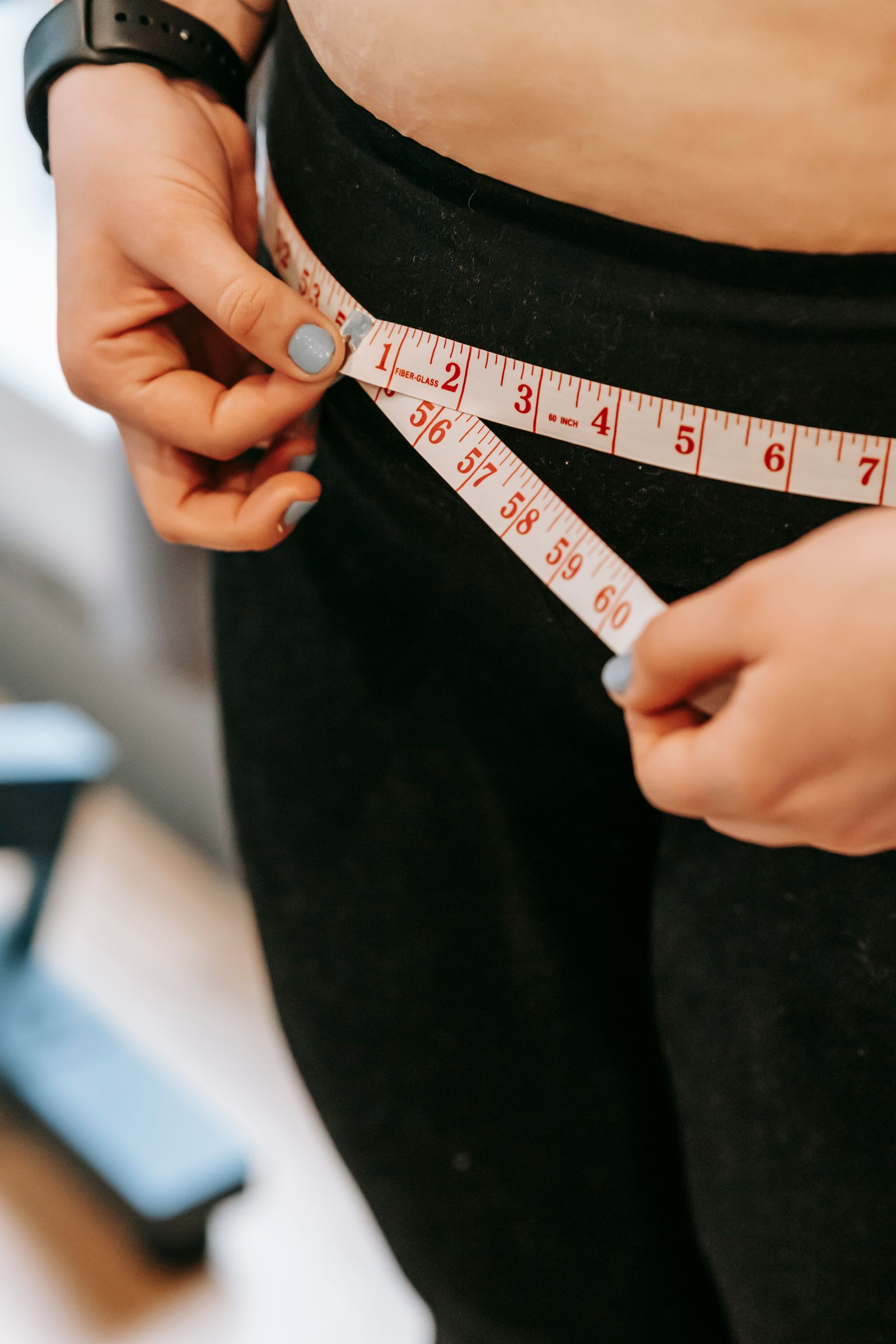 A person measuring their hips with a tape measure in a gym setting