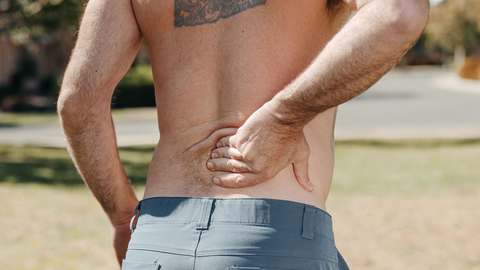 A shirtless man holding his lower back outdoors