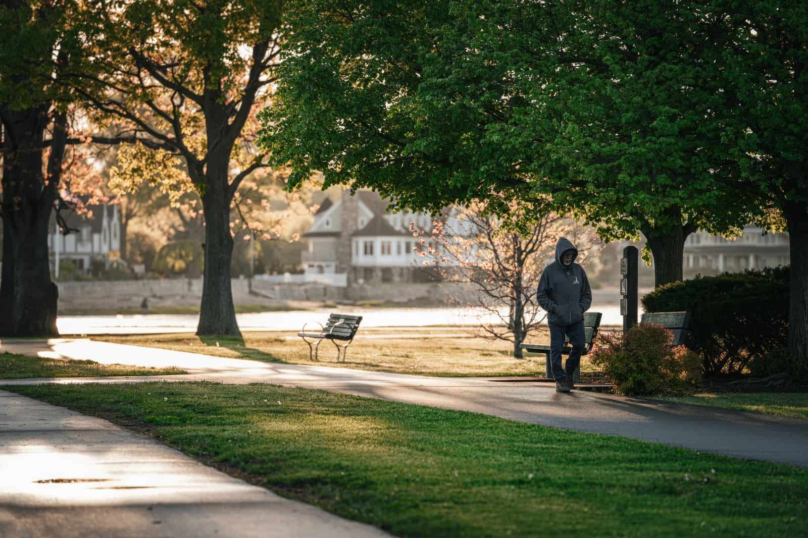 A person walking briskly along a sunlit park path in the morning