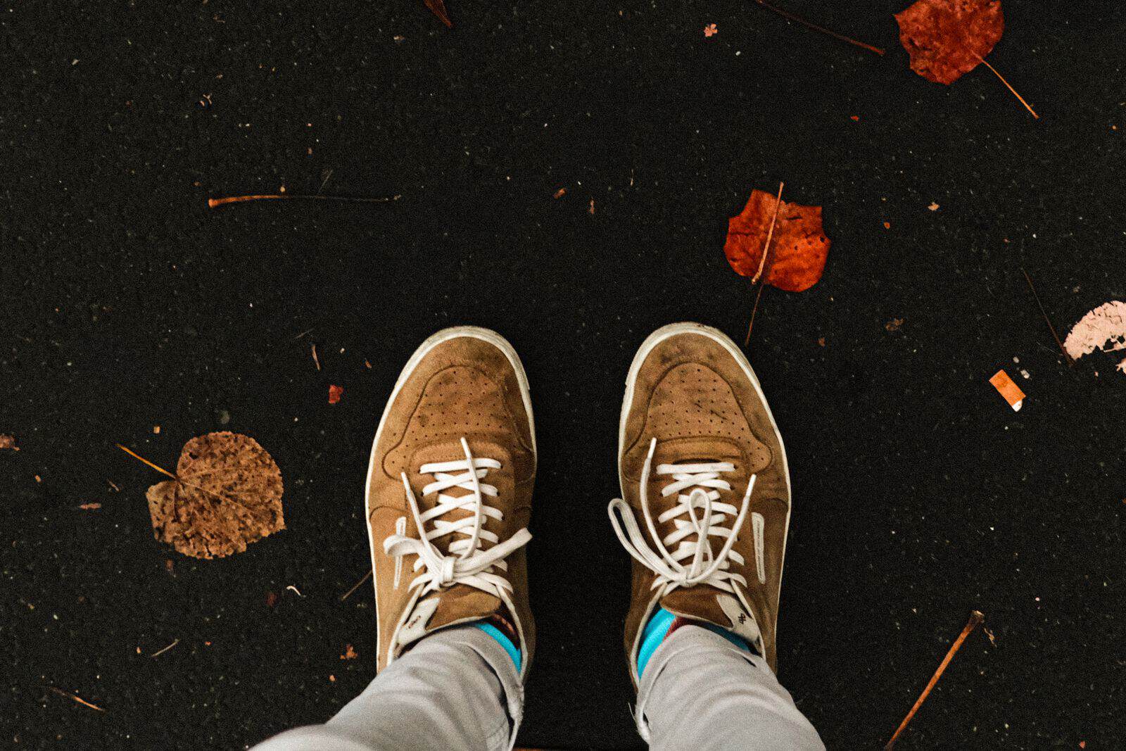 Close-up of sneakers walking through fallen autumn leaves on a path