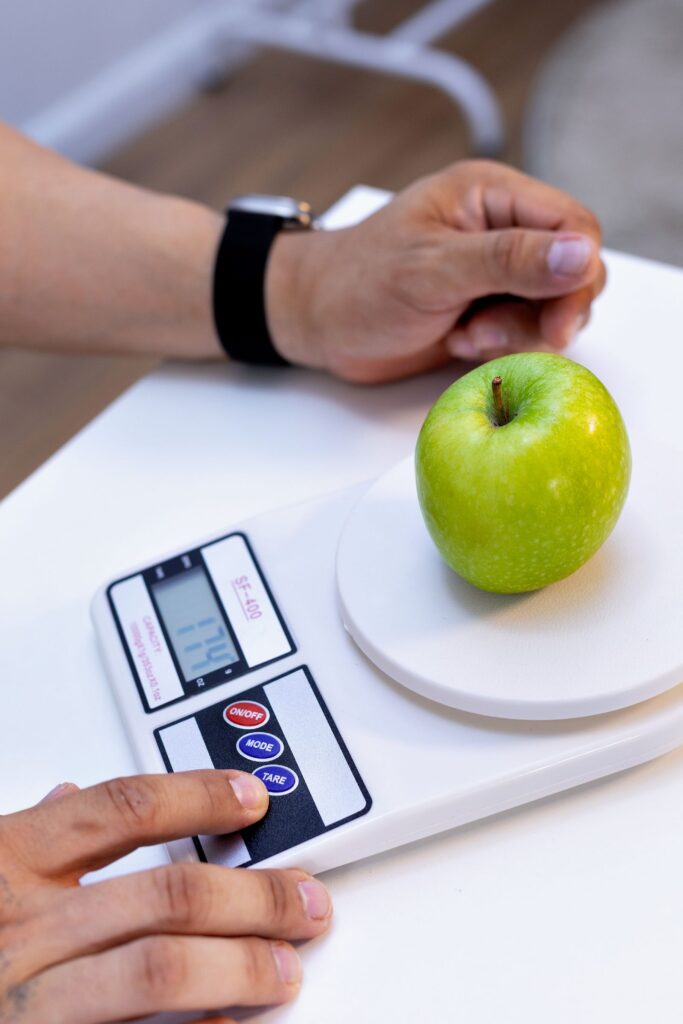 A person weighing a green apple on a digital scale for nutrition tracking