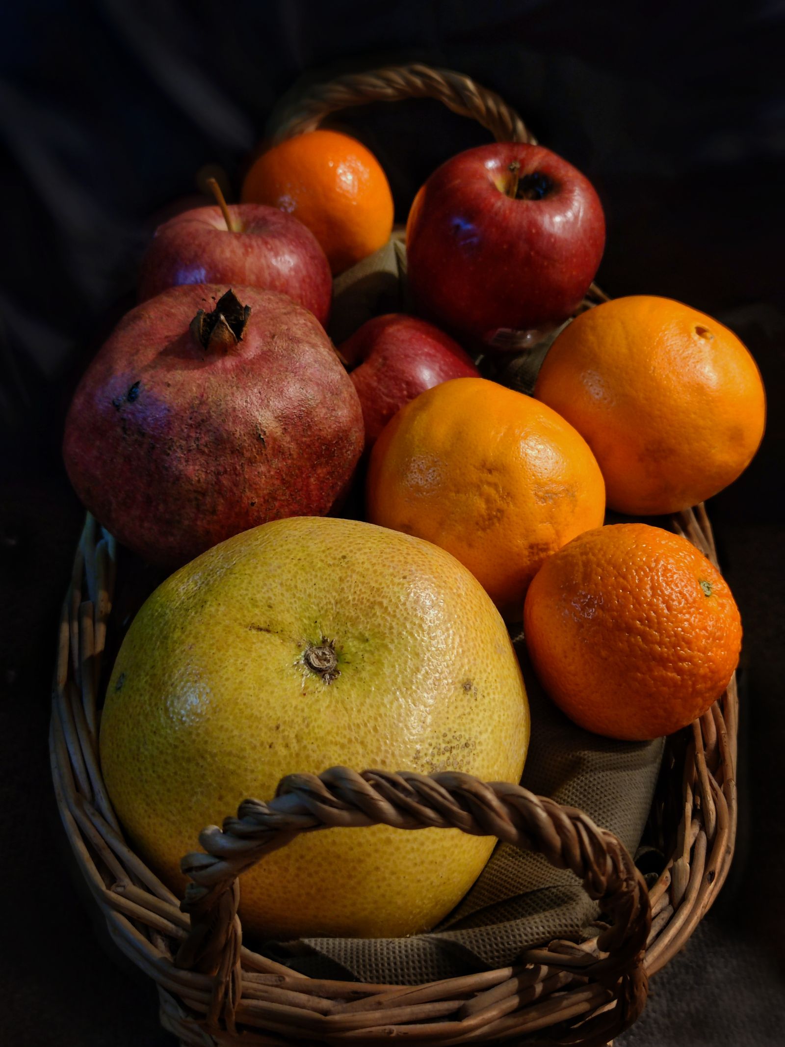 A wicker basket filled with fresh pomegranates, apples, oranges, and grapefruit