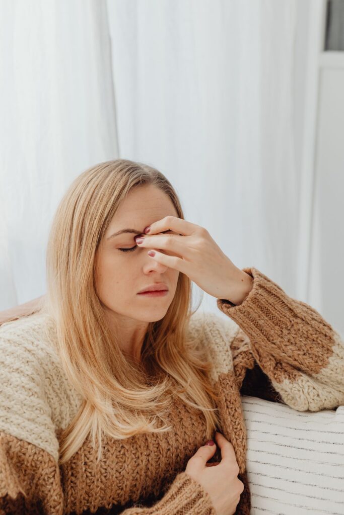 A woman sitting with a headache, wearing a cozy sweater indoors