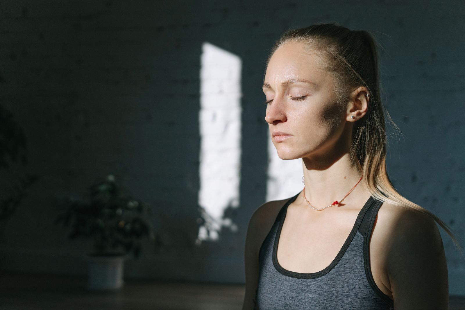 A woman in meditation inside a sunlit room, eyes closed, feeling calm and peaceful