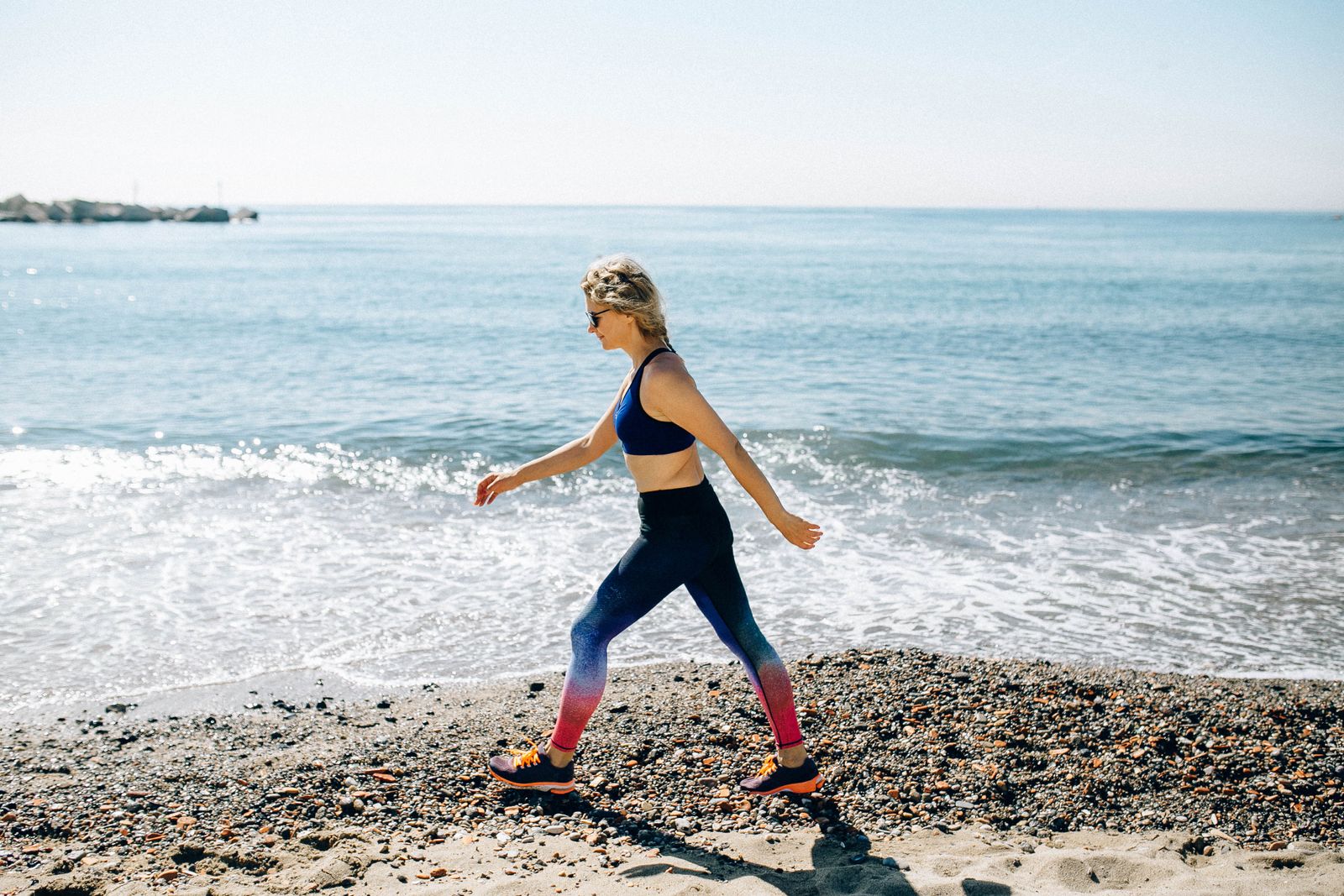 A woman in activewear power walking along a sunny beach shore