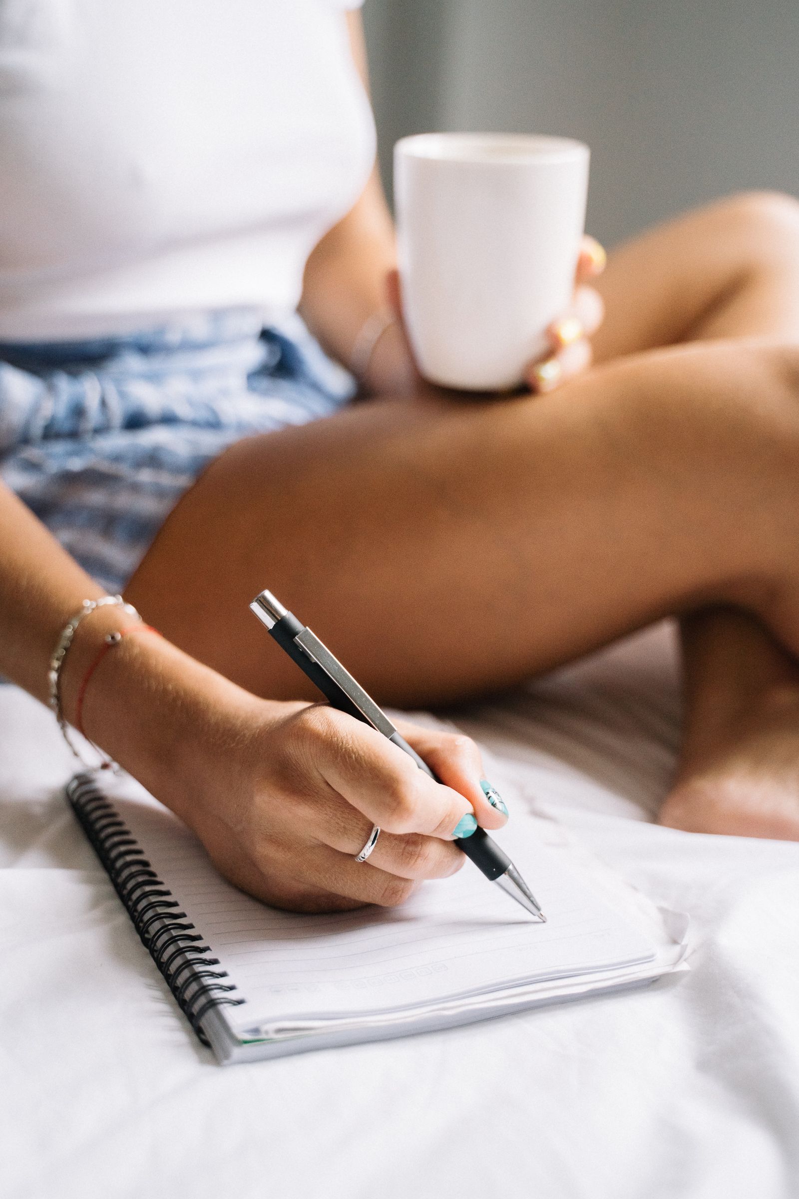 A woman enjoying a calm morning, drinking coffee and writing in a notebook while sitting in bed