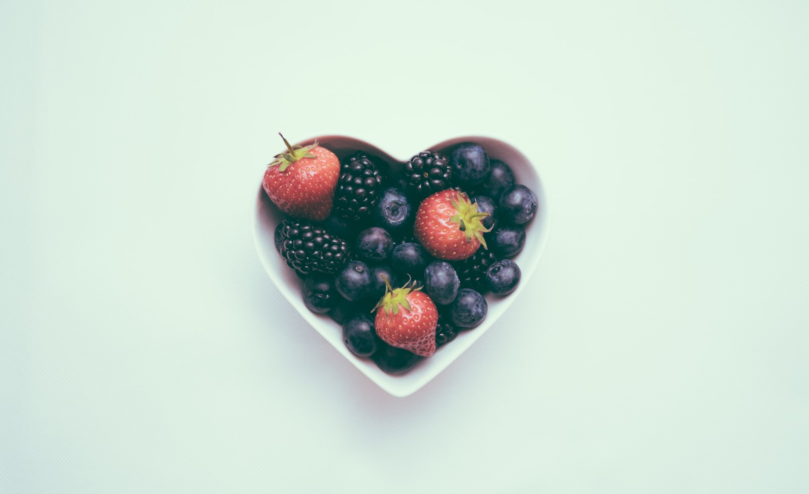 A heart-shaped bowl filled with fresh strawberries